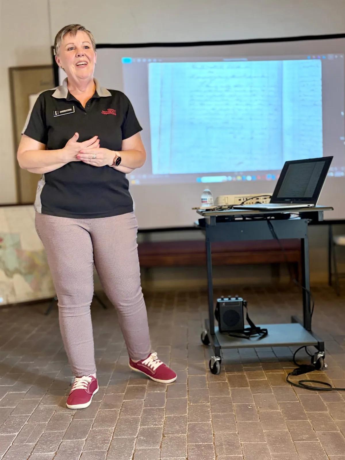Machelle Wood speaking beside a projected historical document